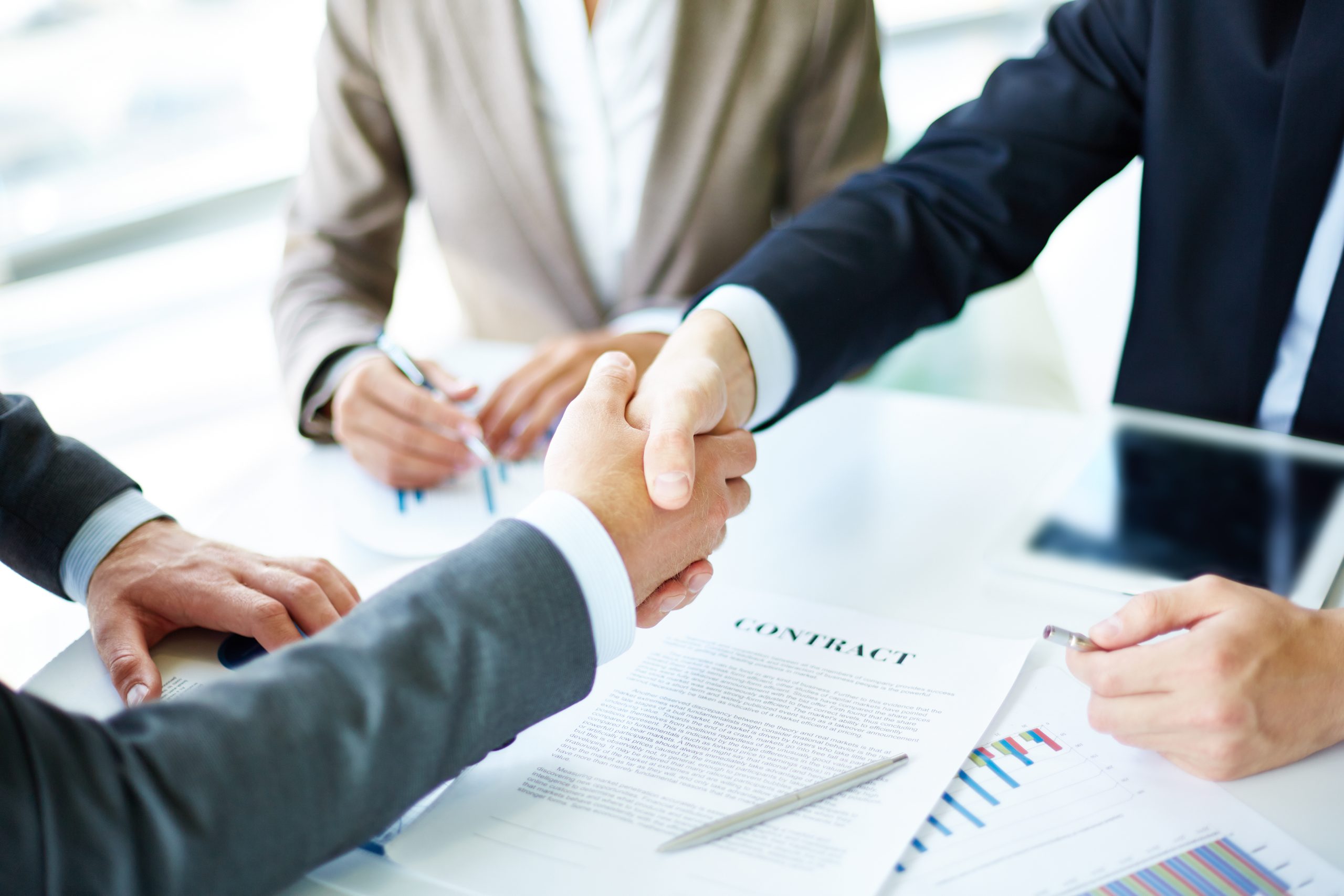 Two advisors shaking hands over a signed contract