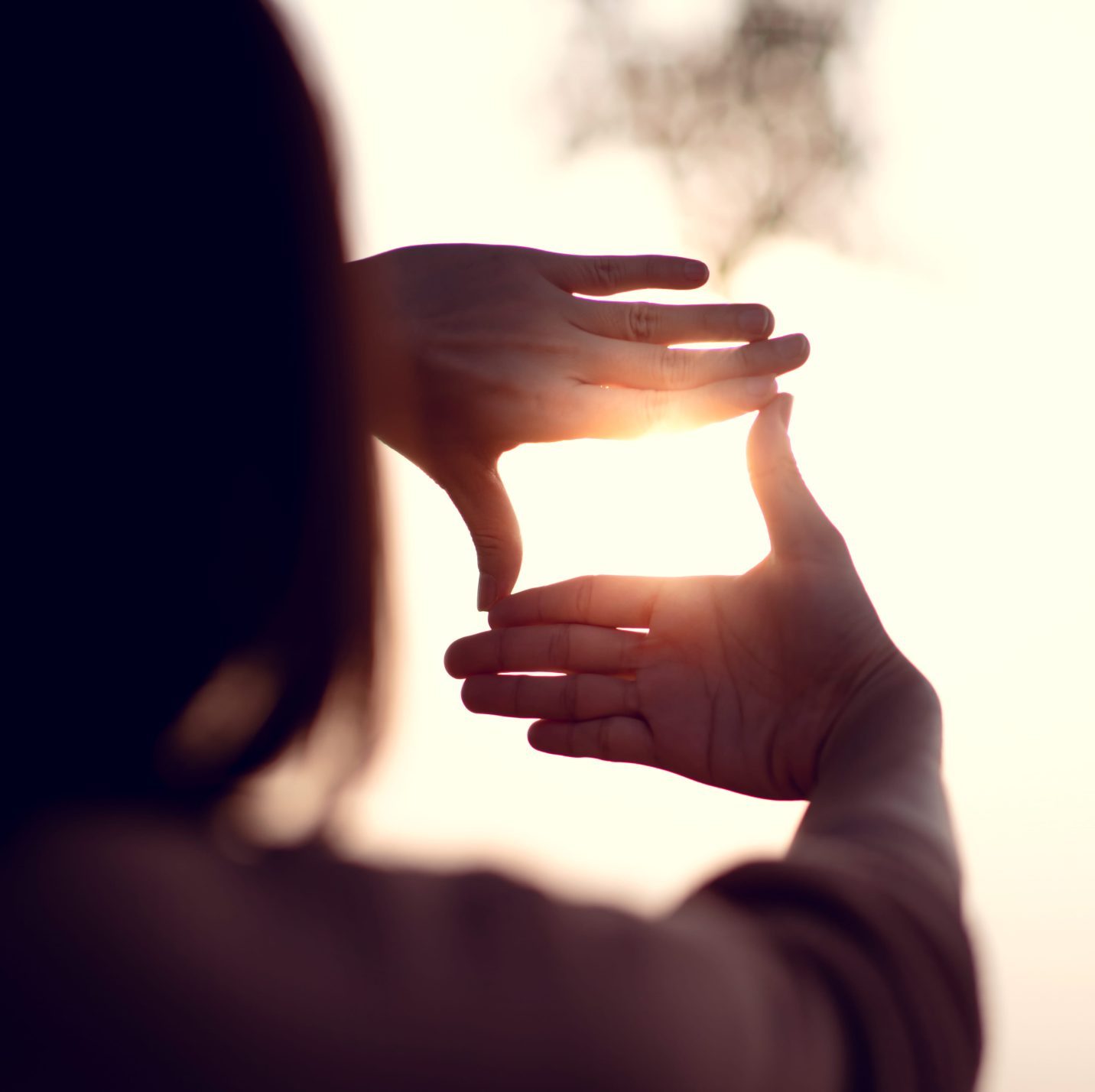 Hands forming a frame around a bright sunrise