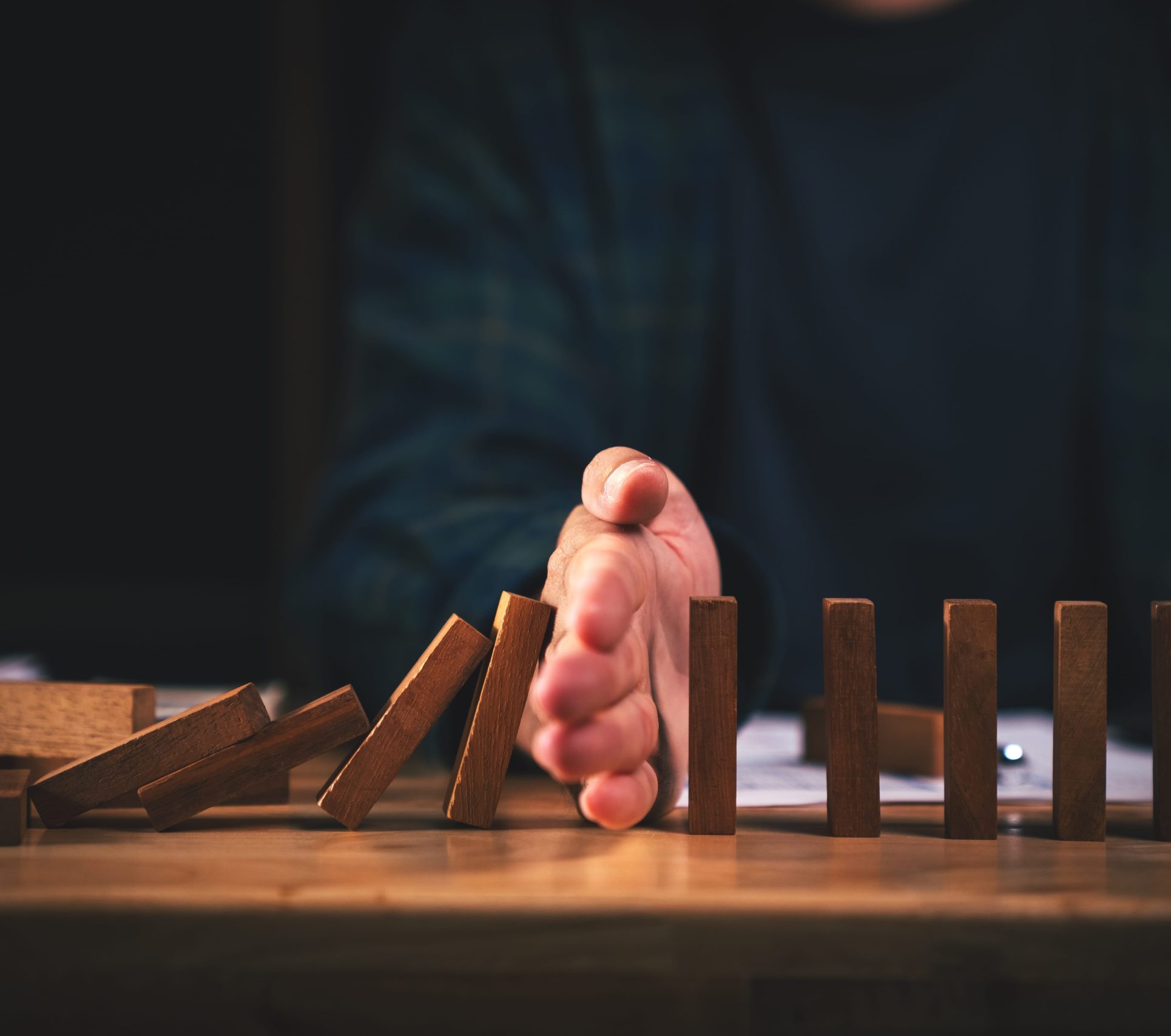 A hand stopping a row of falling wooden dominoes