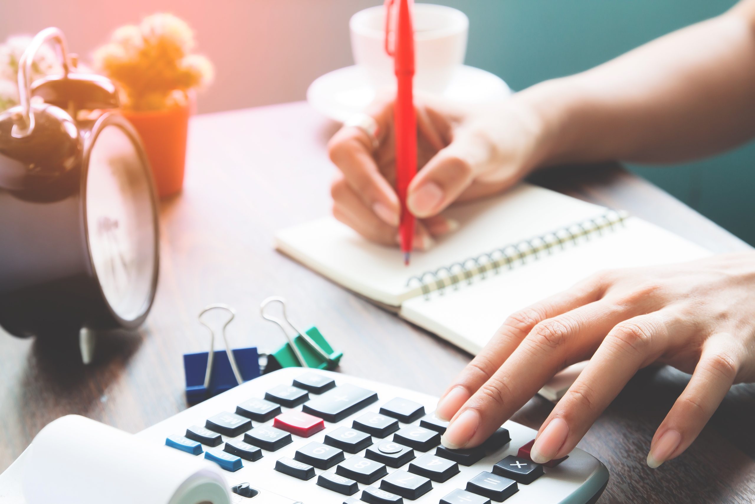 A person writing in a notebook while using a calculator