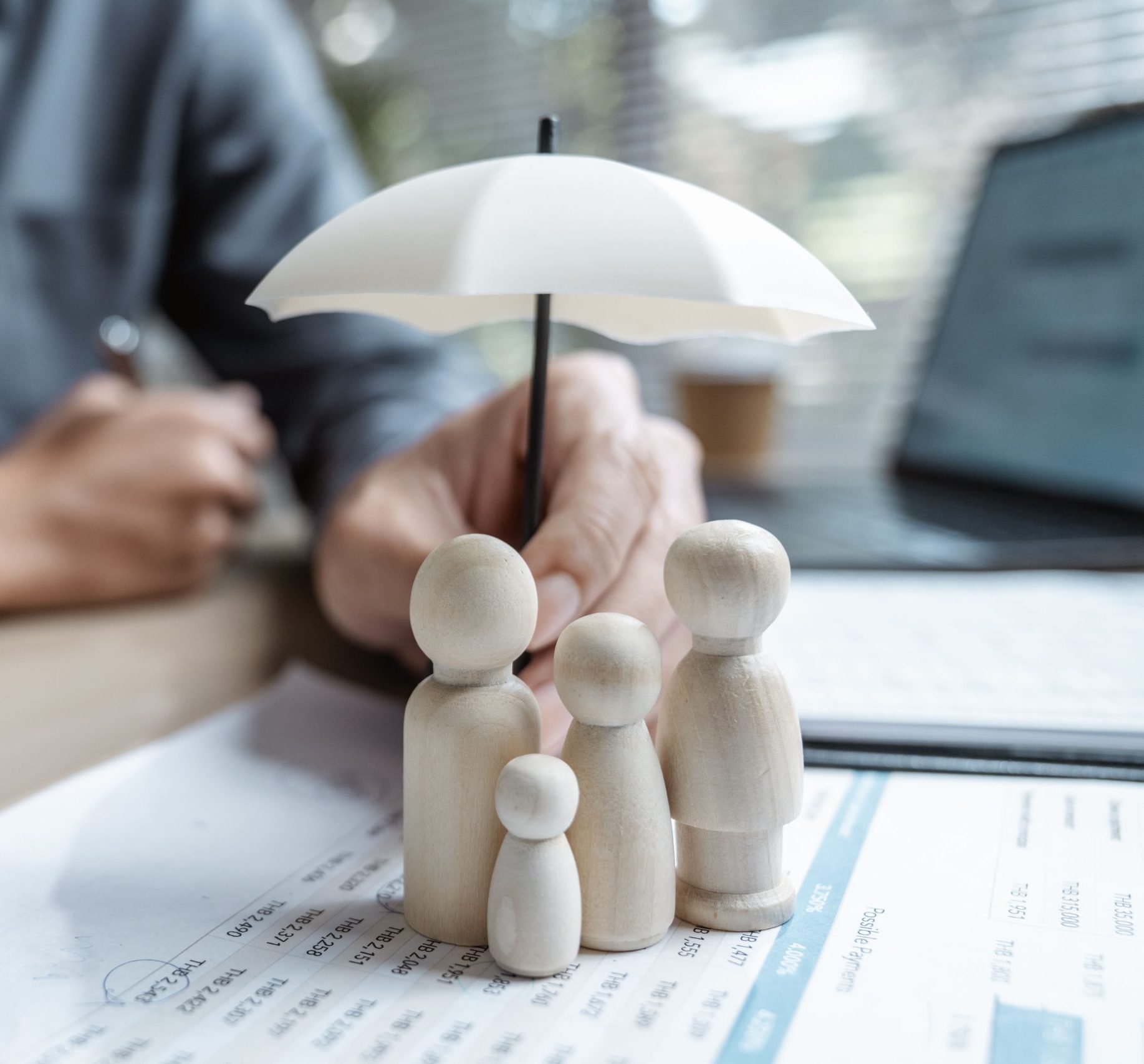 A small umbrella held over wooden family figures on financial papers