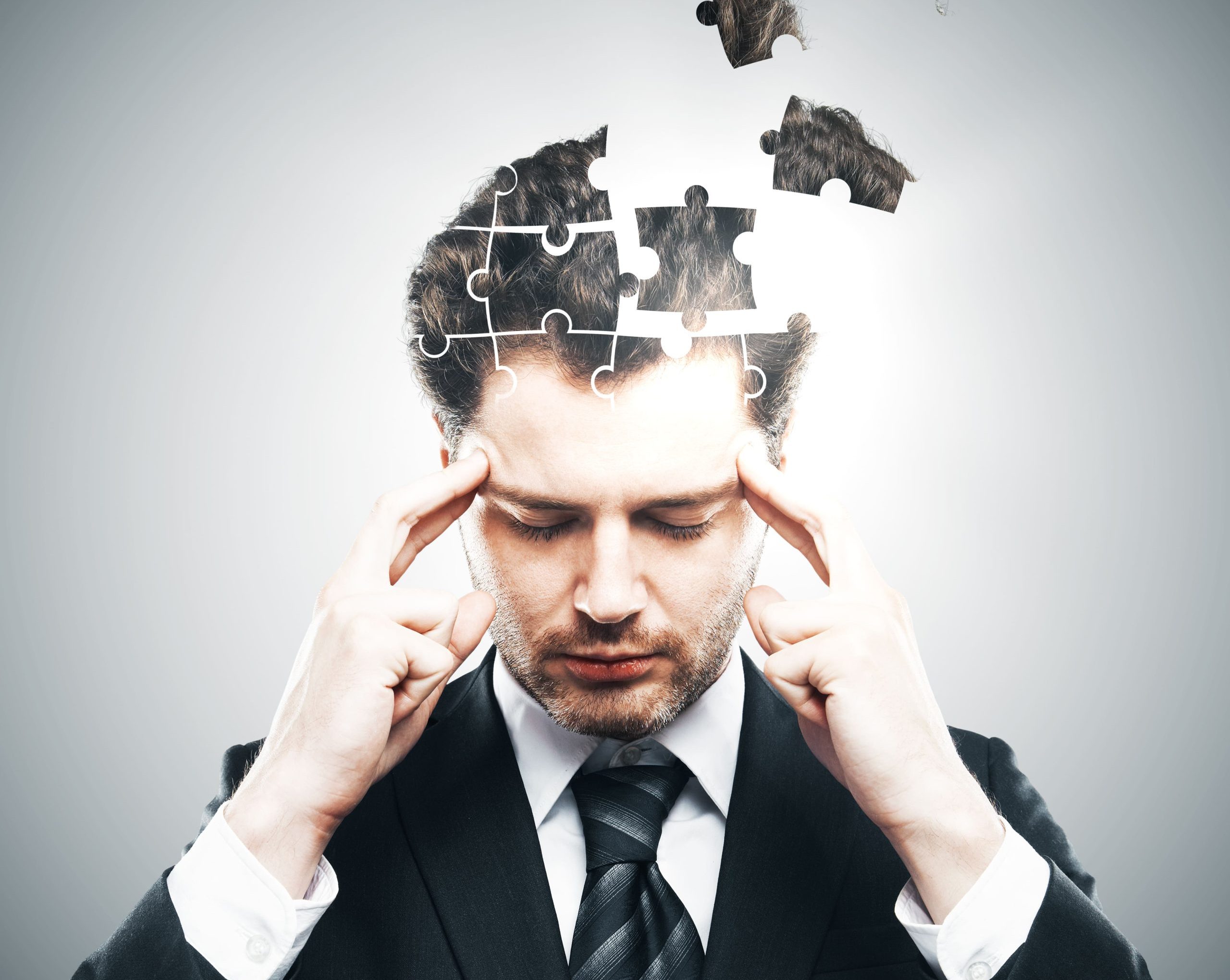 A businessman holding his head as puzzle pieces break away